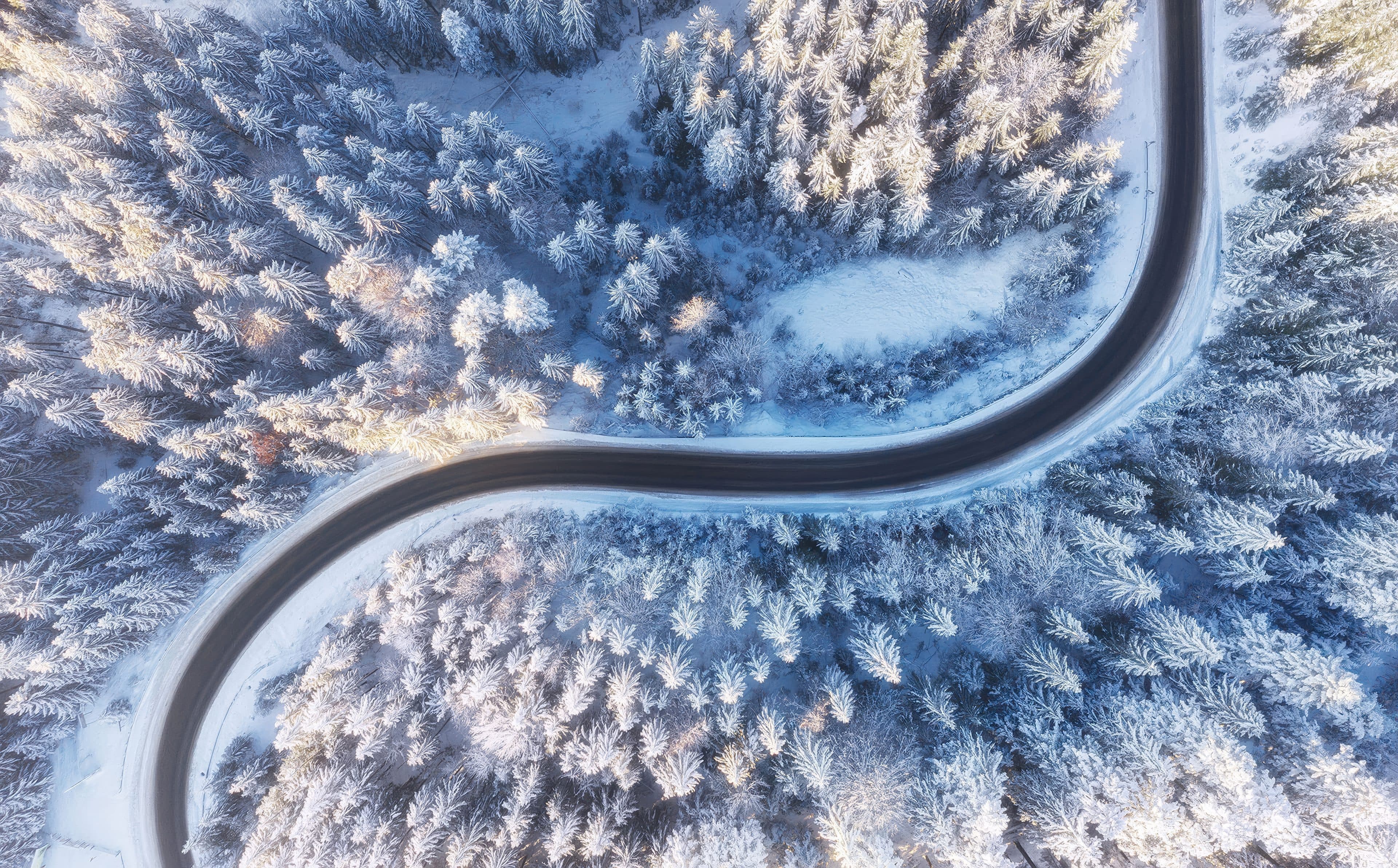 Aerial view of a winter road winding through snow-covered forest