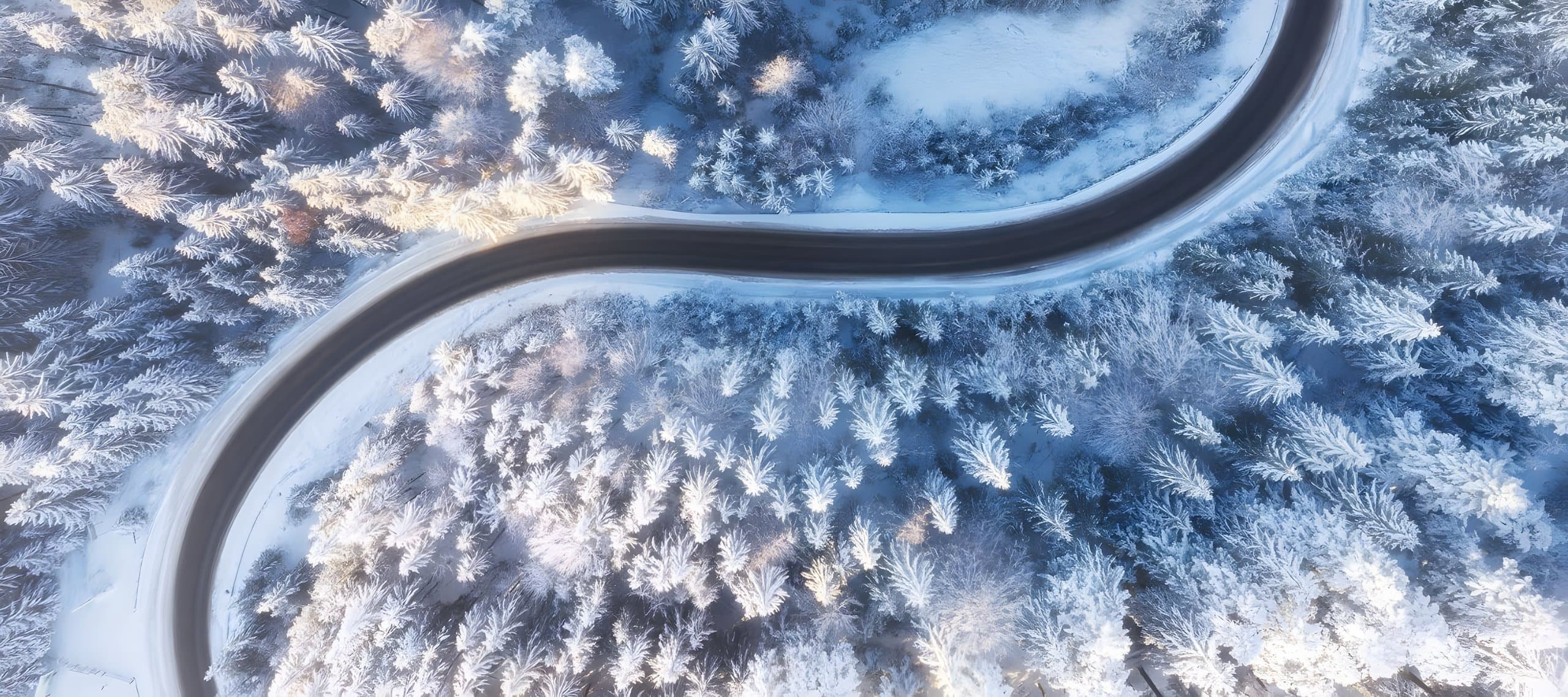 Aerial view of a road curving through snow-covered forest